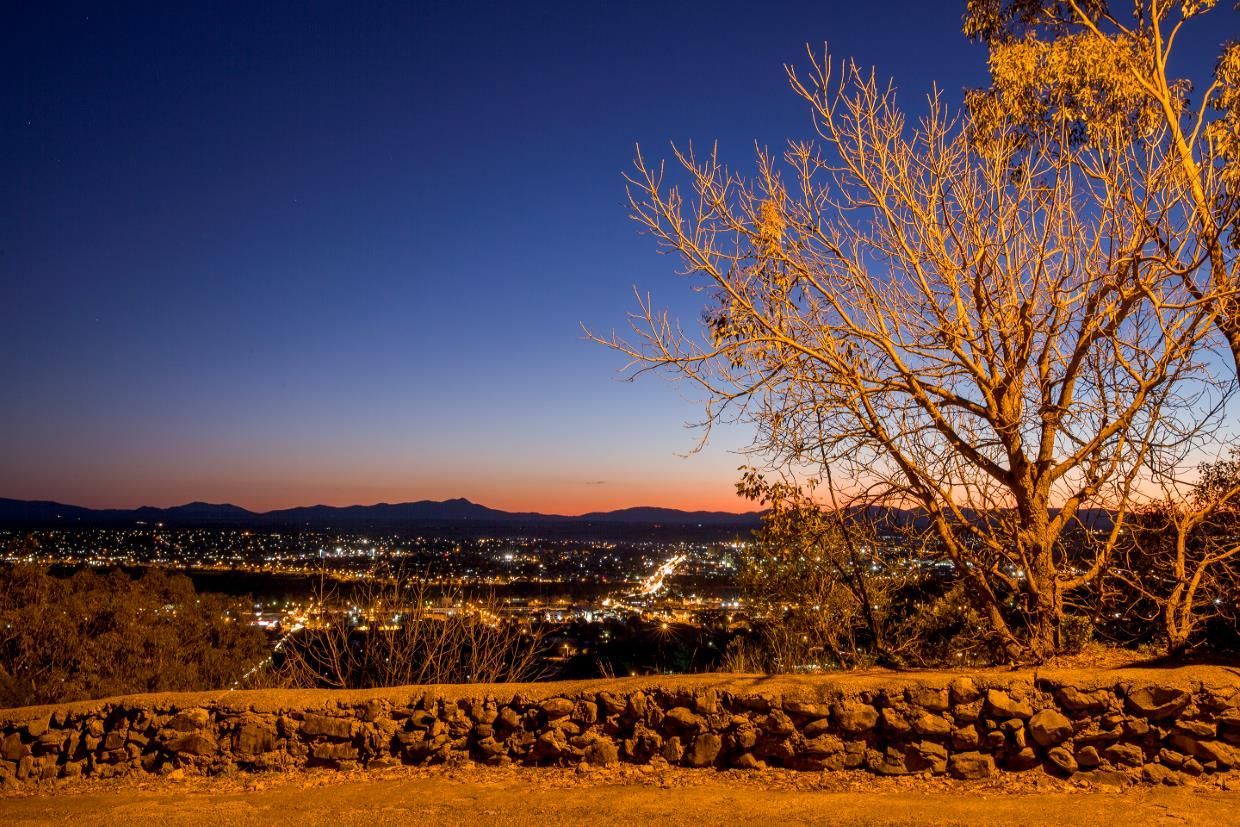A Tree Stands in Front of A Stone Wall Overlooking a City at Sunset — New England Shade Sails in Tamworth, NSW