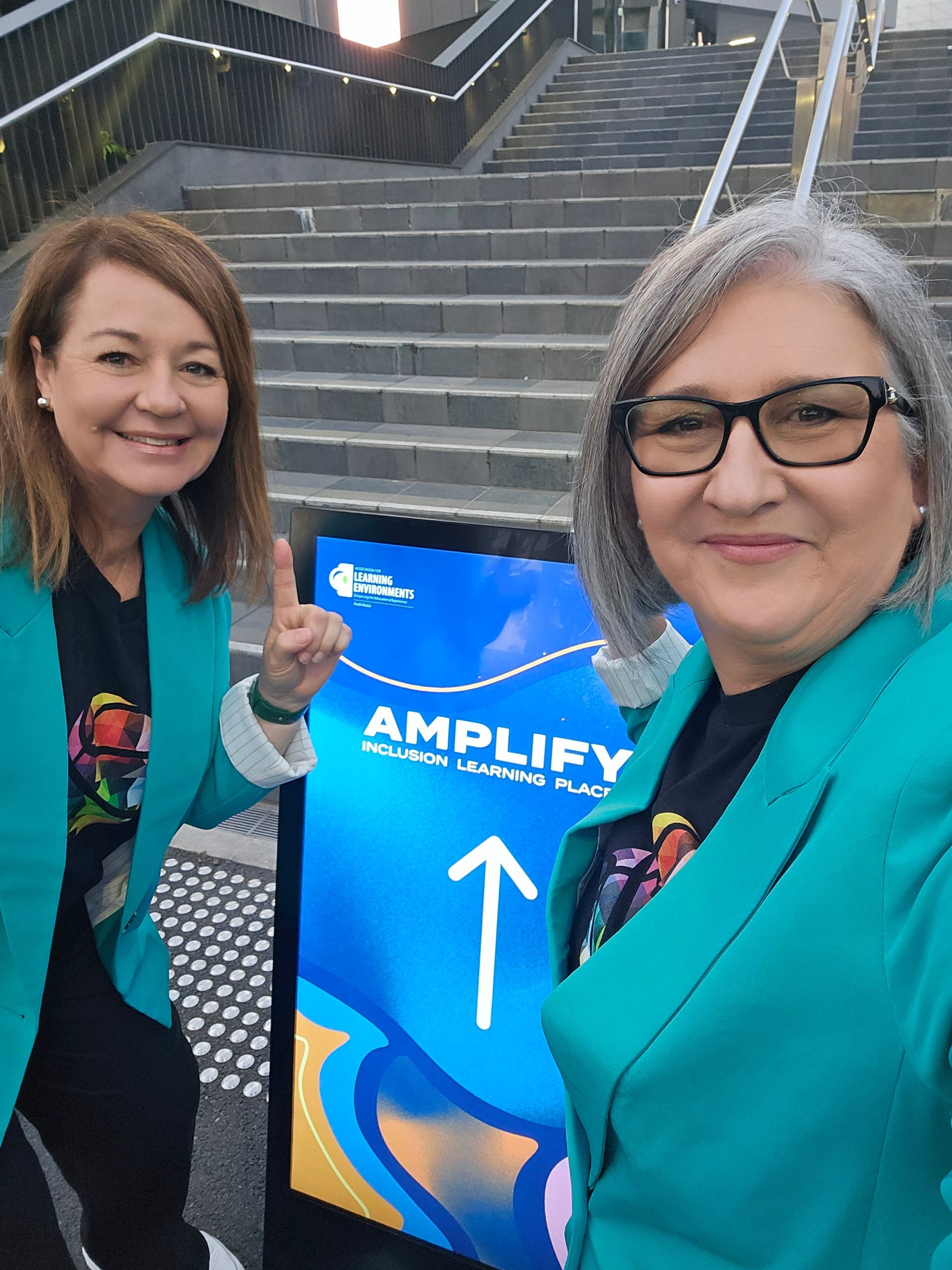 Two women standing next to a sign that says amplify