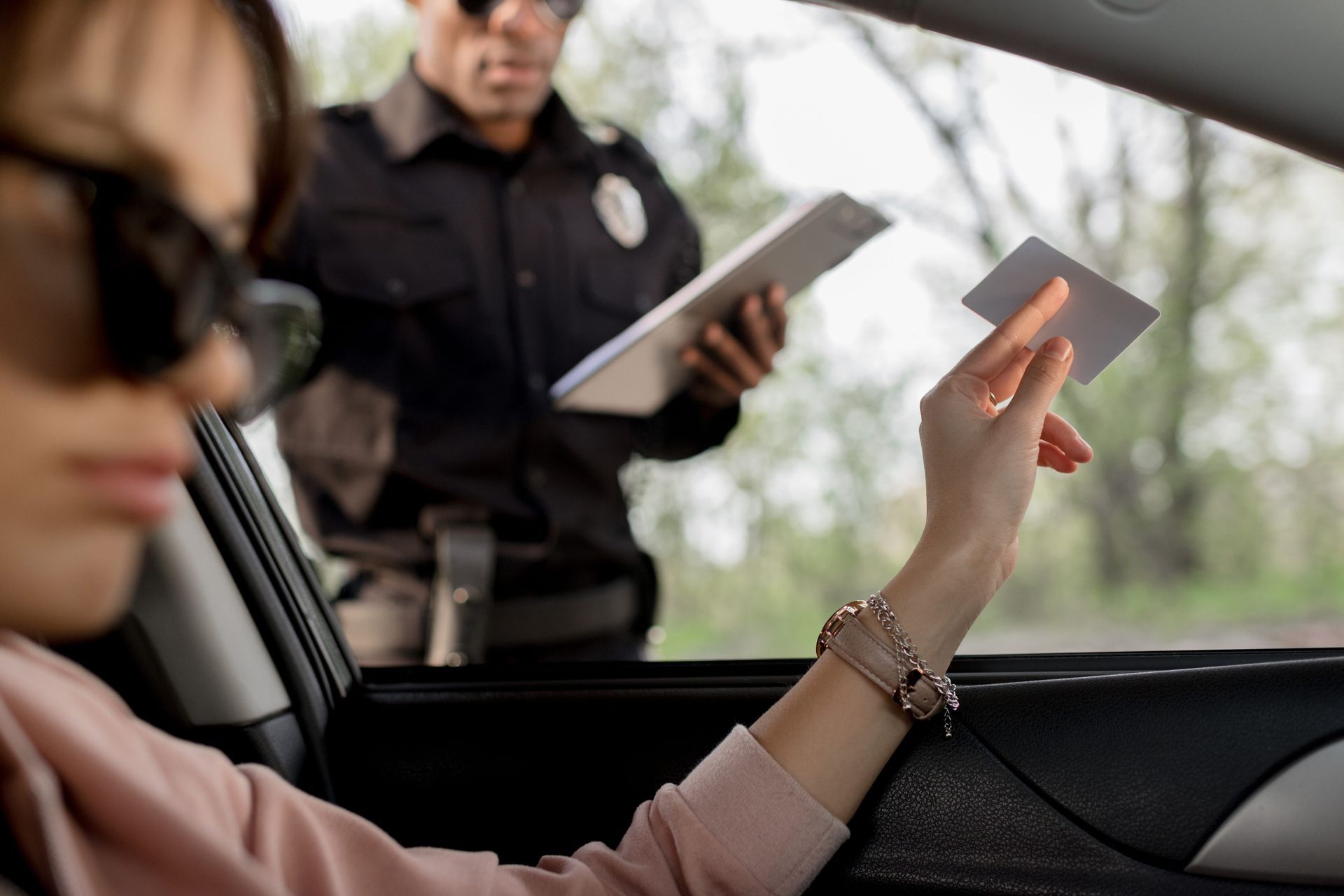 Police officer checks ID through a car window while passenger holds it up.