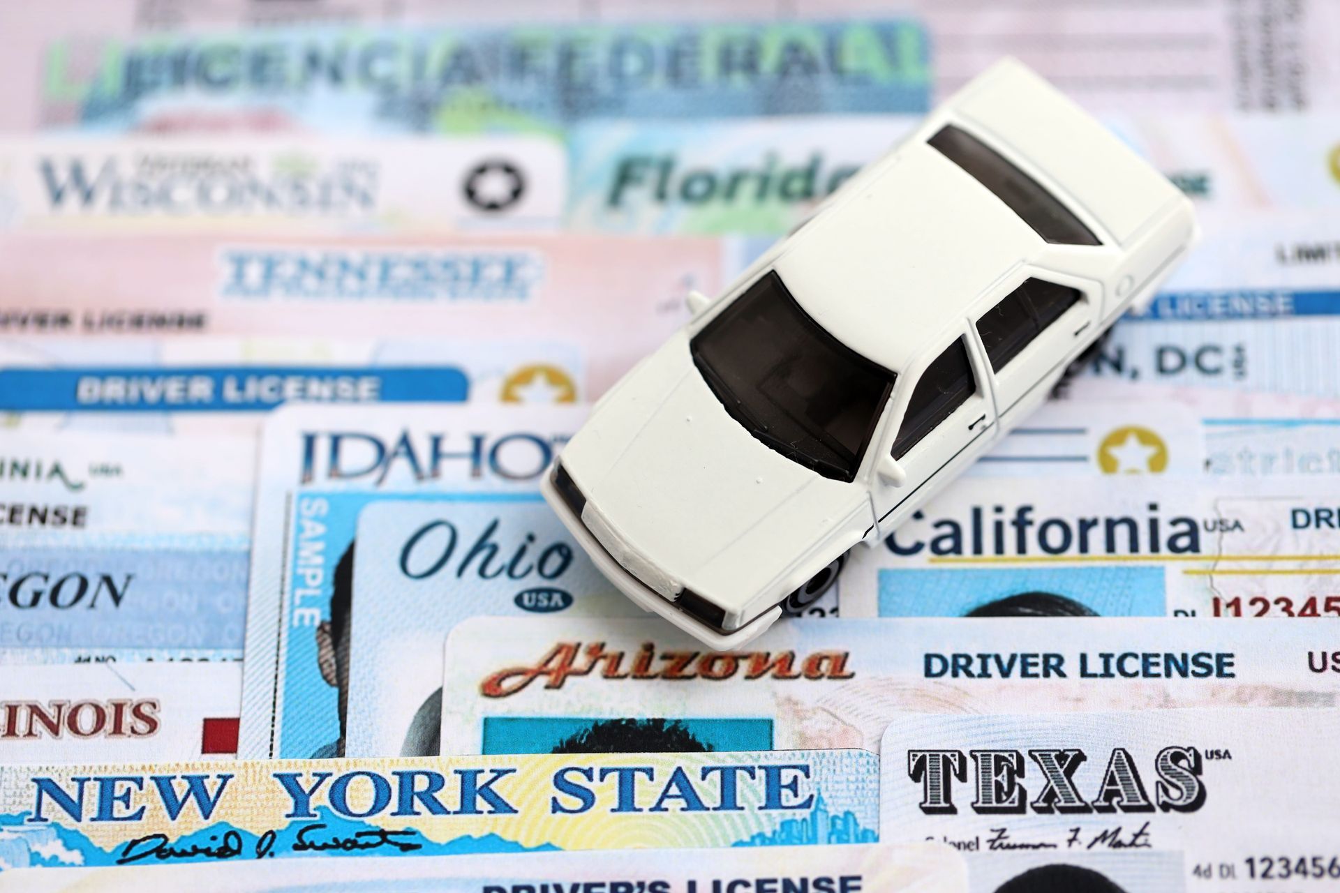 White car on a collage of U.S. driver’s licenses, suggesting driving or auto insurance concepts