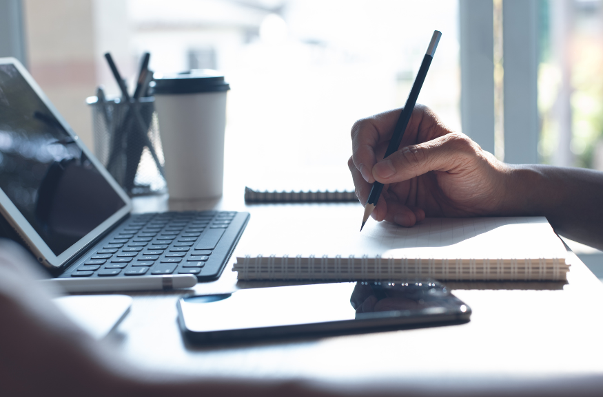 A person is sitting at a desk writing in a notebook.