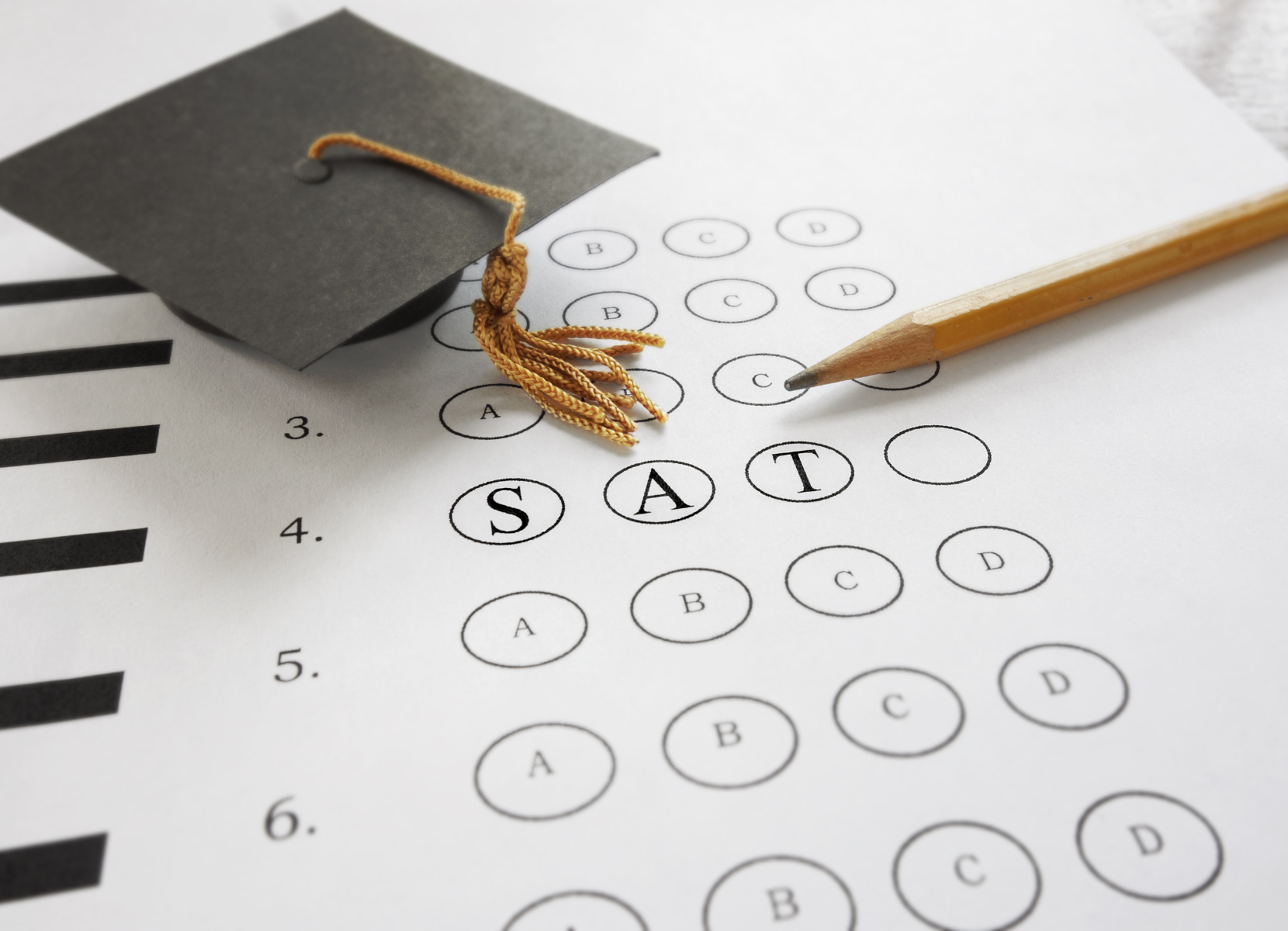 A graduation cap and a pencil on top of a sat test