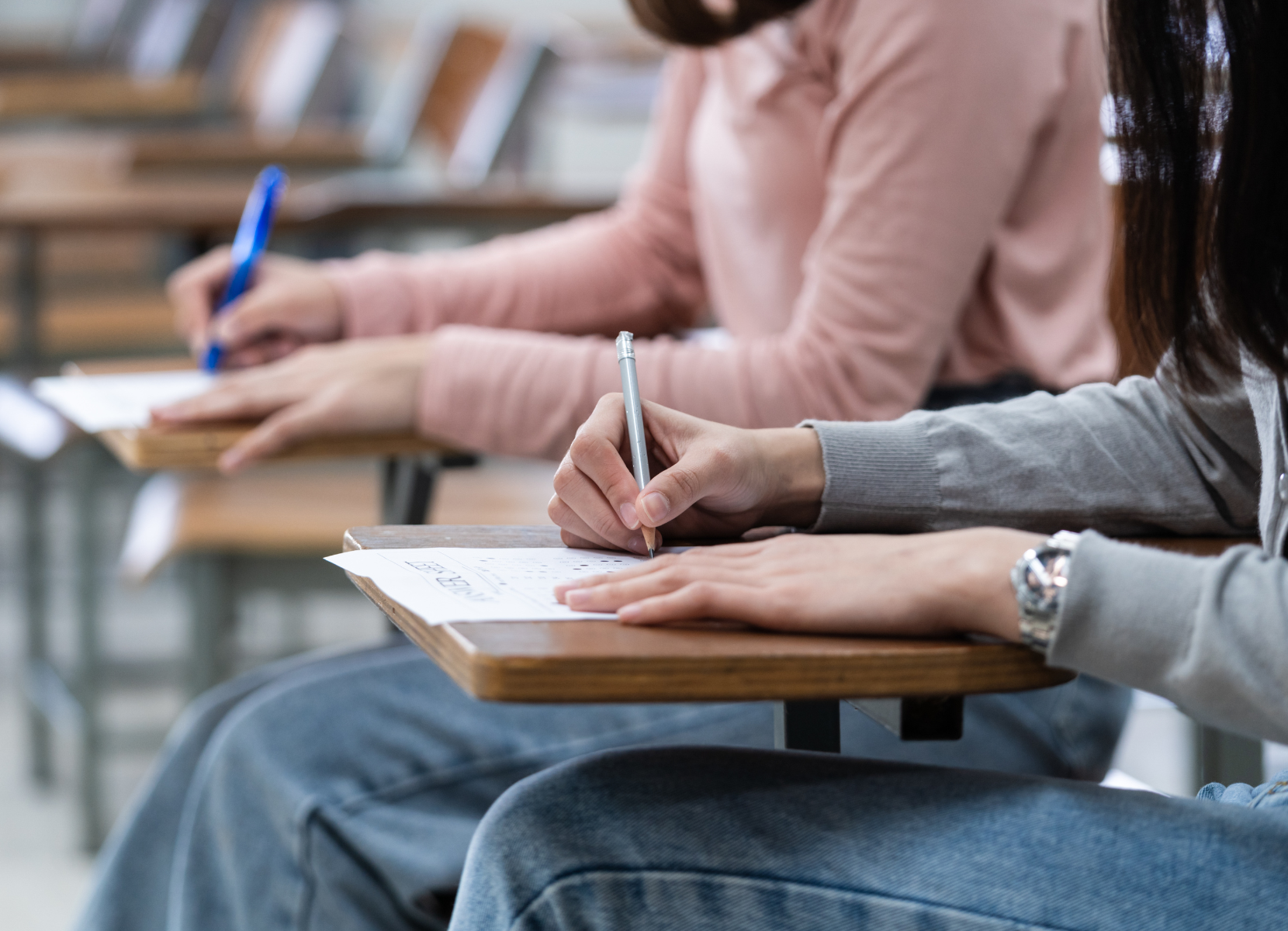 A group of people are sitting at desks in a classroom writing on papers.