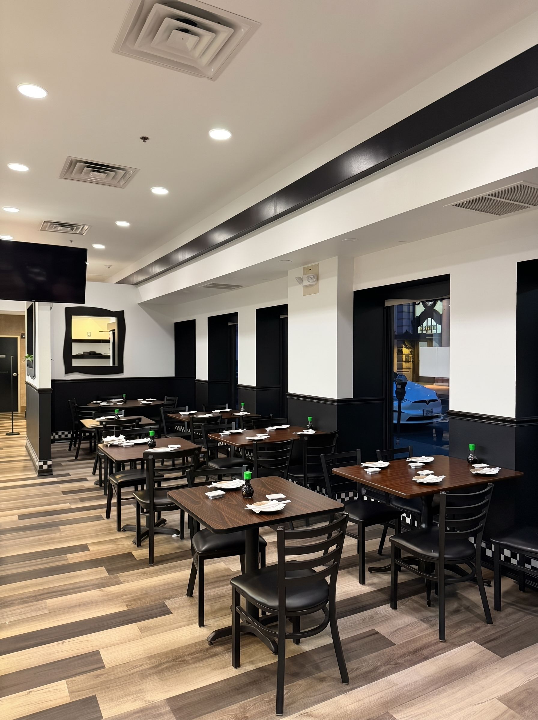 Empty modern restaurant dining area with black chairs, wooden tables, and striped flooring