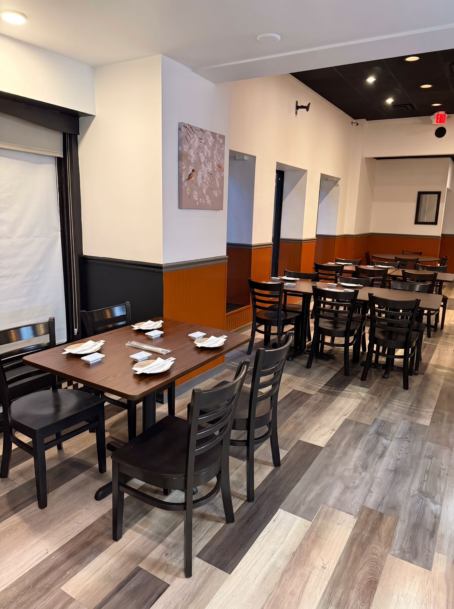 Empty restaurant dining room with dark wood tables, black chairs, and gray wood-look floors