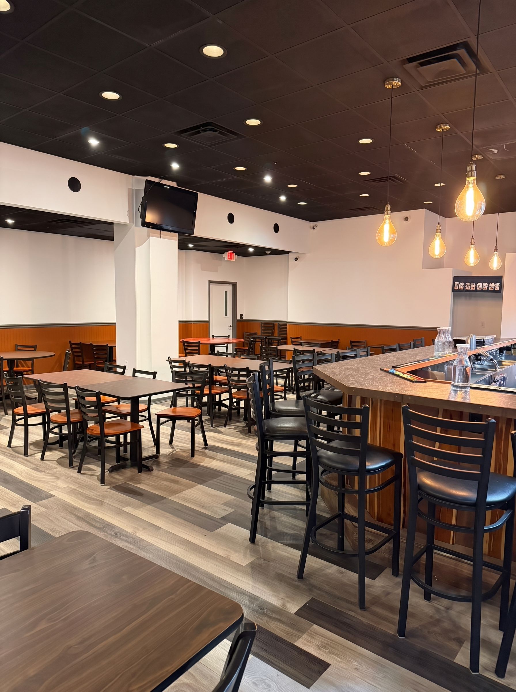 Empty modern restaurant interior with tables, stools, pendant lights, and a bar area