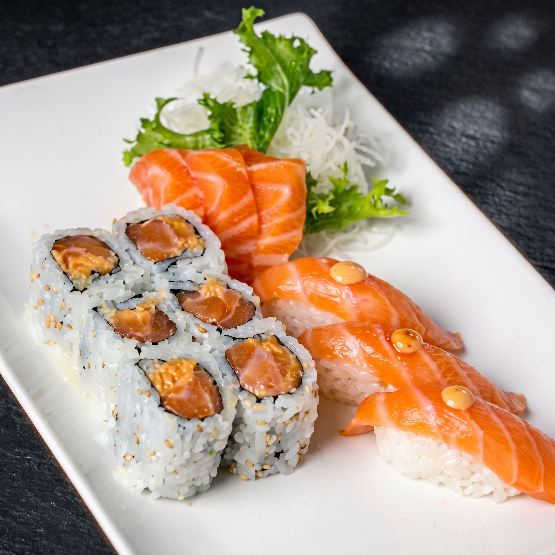 Sushi platter with salmon nigiri, sushi rolls, and greens on a white plate