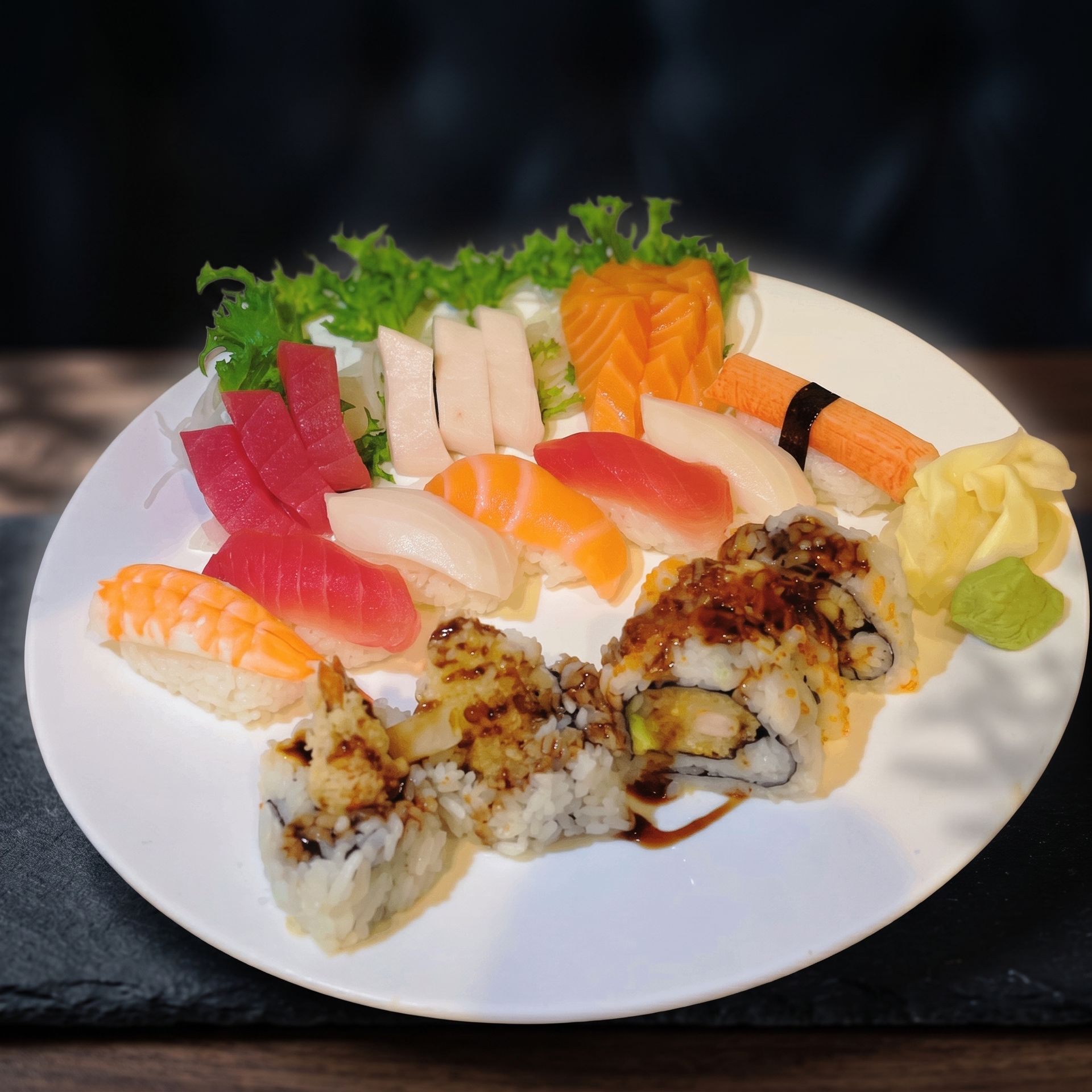Assorted sushi rolls and sashimi arranged on a white plate with garnish and dipping sauce