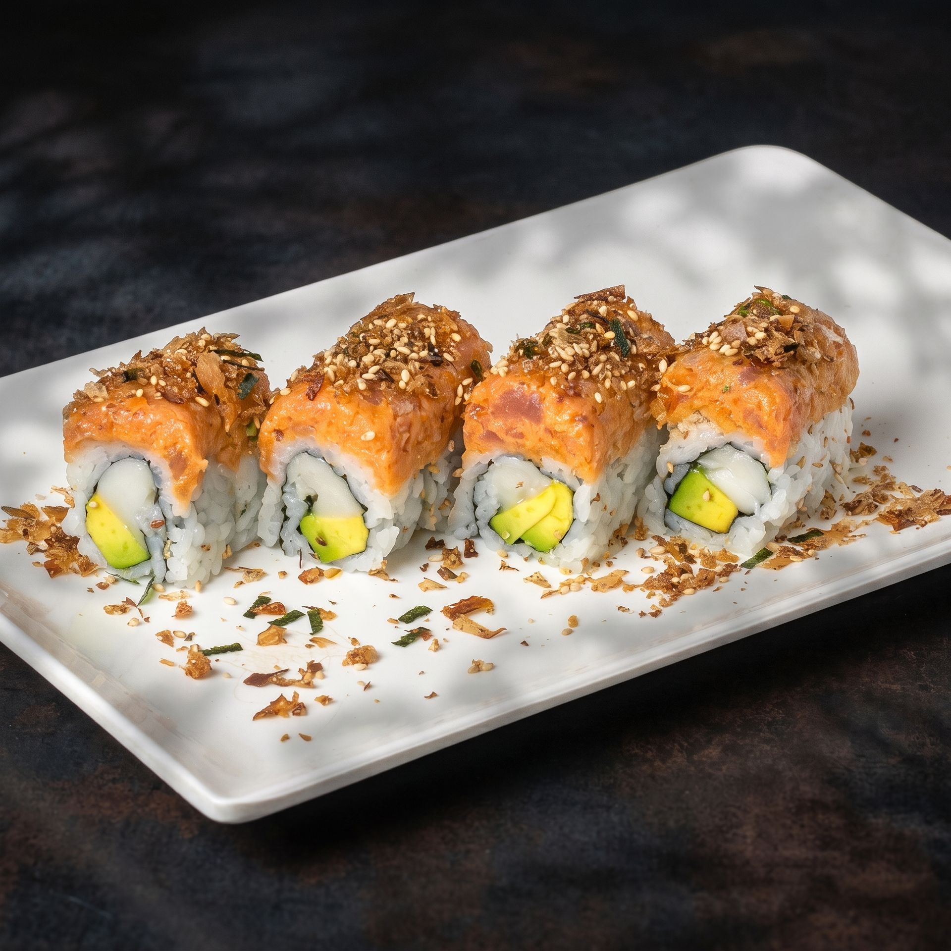 Sushi rolls topped with orange sauce and sesame seeds on a white rectangular plate