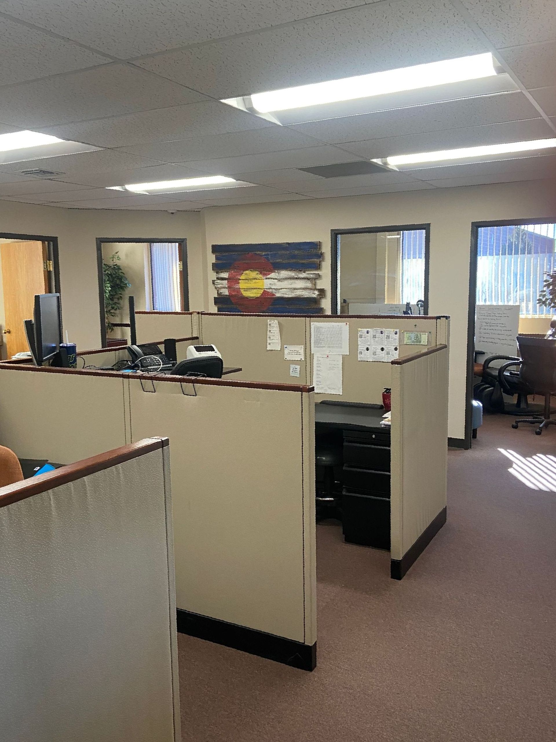 Office cubicles with beige partitions, fluorescent lights, and desks in a carpeted workspace