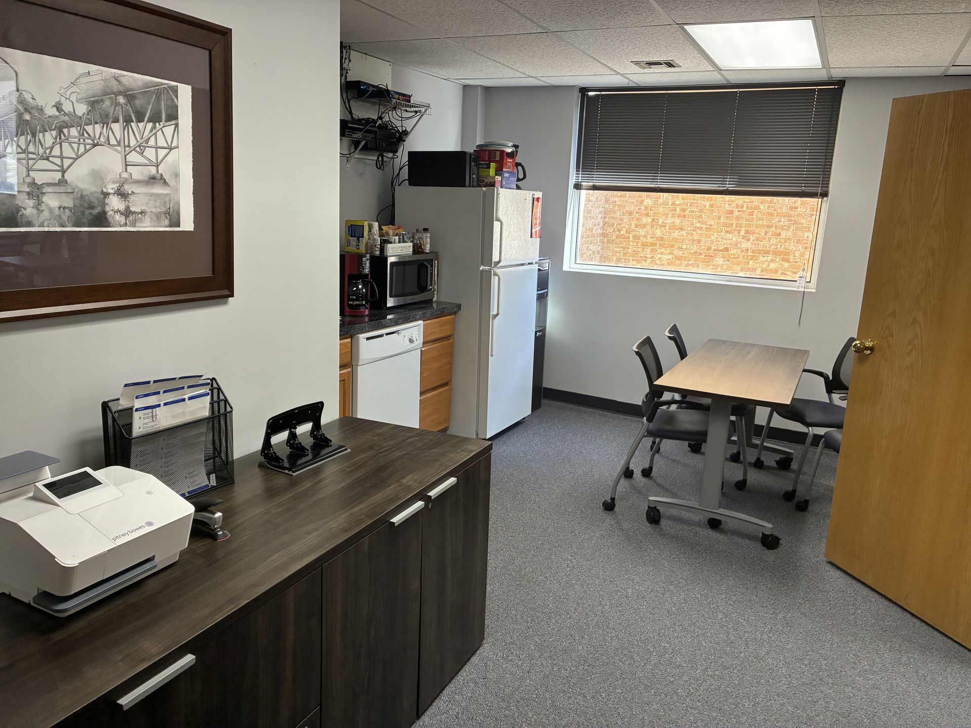 Small office break room with table, chairs, mini fridge, microwave, and printer.