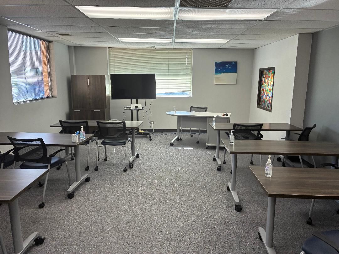Empty classroom with desks, TV, and window blinds in a carpeted room