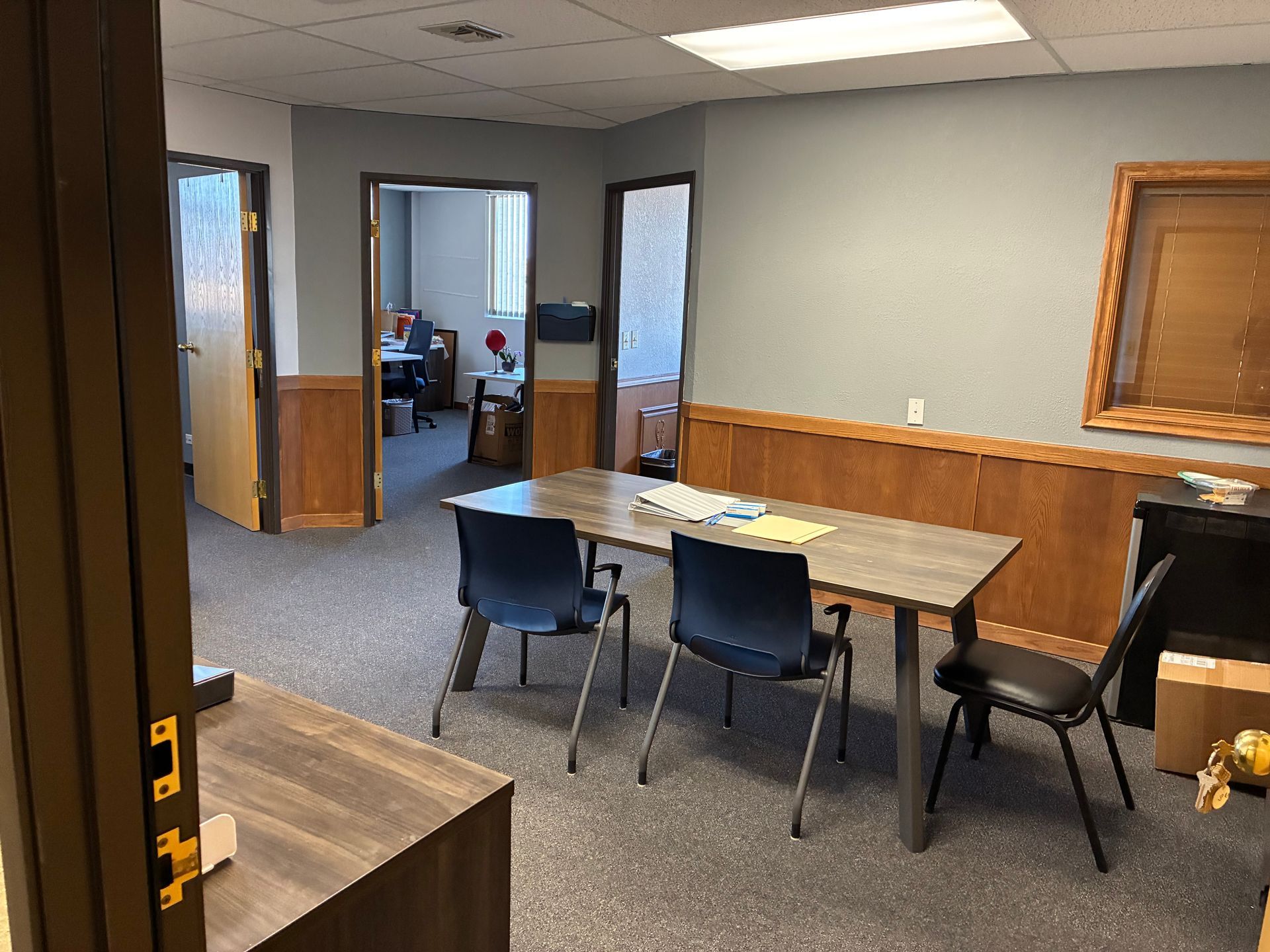 Empty office meeting room with tables, chairs, and a windowed doorway in the back.