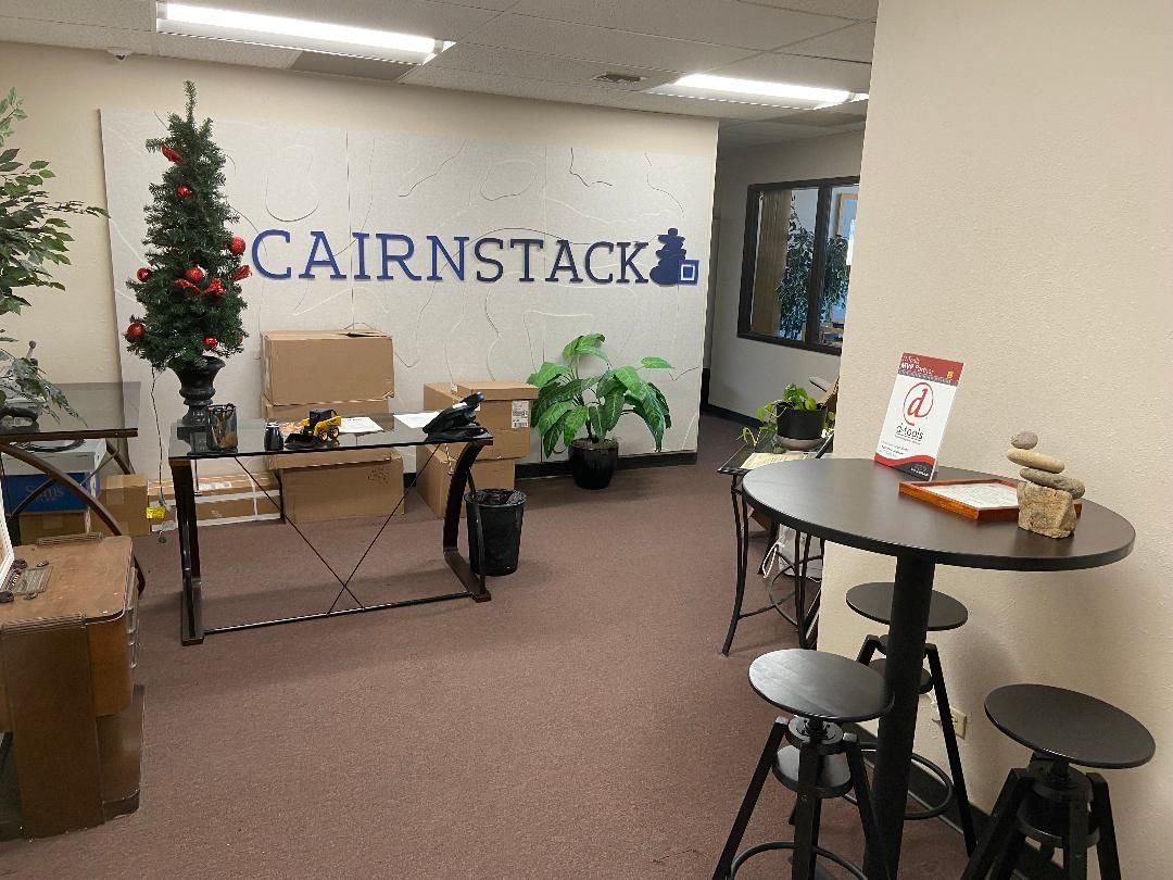 Office lobby with CAIRNSTACK sign, decorated Christmas tree, desks, and small table with stools