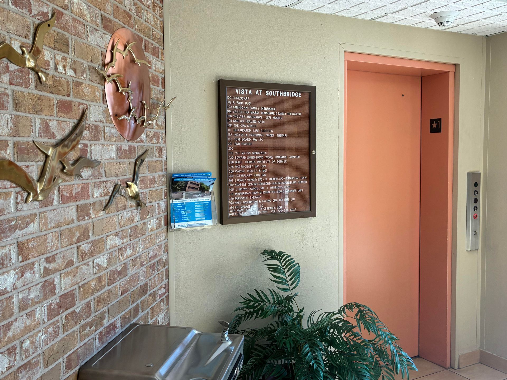 Office hallway with elevator, wall art, directory board, and potted plant