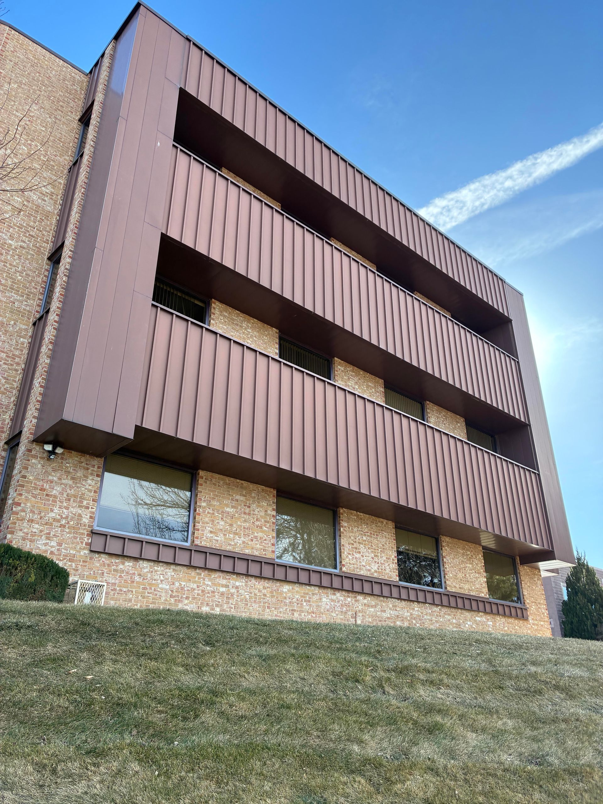 Low-rise apartment building with brown balconies and stone facade under a blue sky