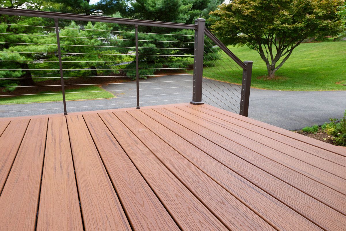 Wooden deck with cable railing overlooking a green lawn and path.
