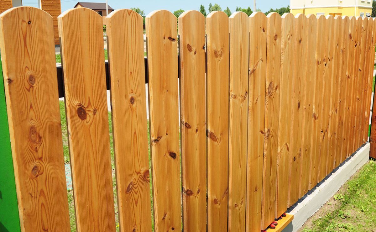 Wooden picket fence with a curved top, in a grassy yard.