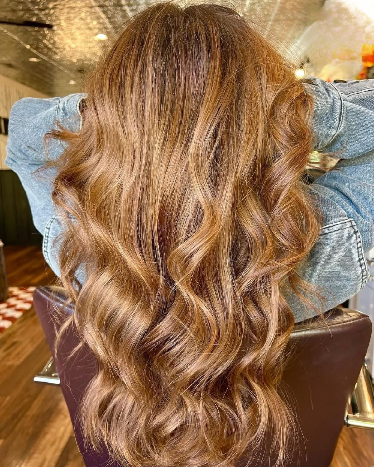 Long, wavy, light brown hair styled with highlights. Person in a denim jacket, seated.