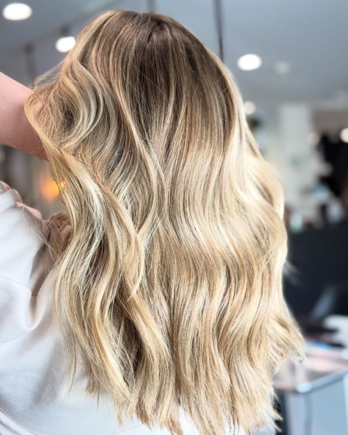 Wavy blonde hair with darker roots, styled for a layered look.