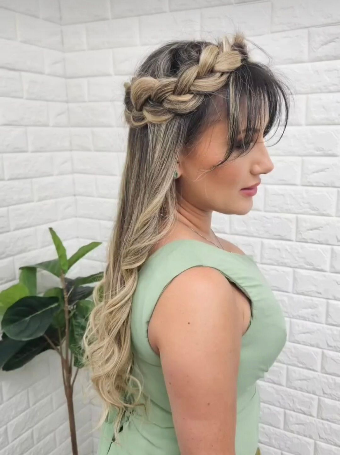 Woman with blonde wavy hair, wearing a braided crown, with bangs and a green dress.