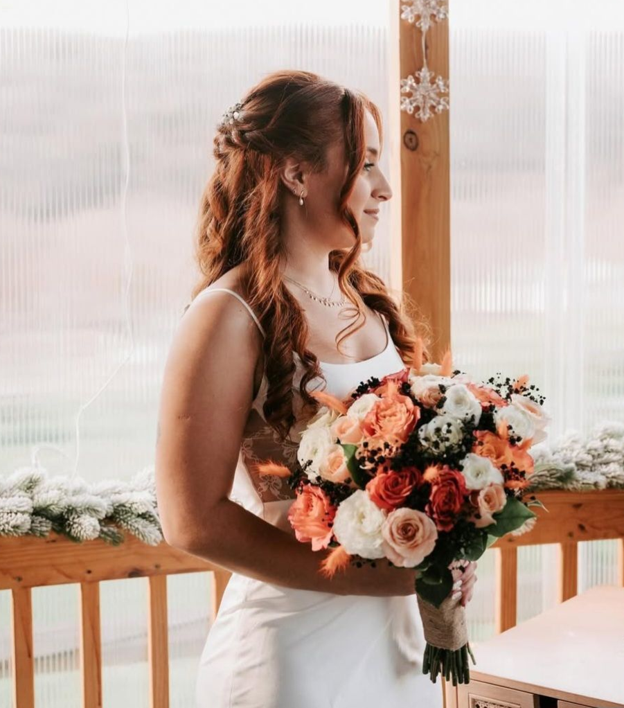 Woman in wedding dress holding bouquet, looking out at a scenic view.