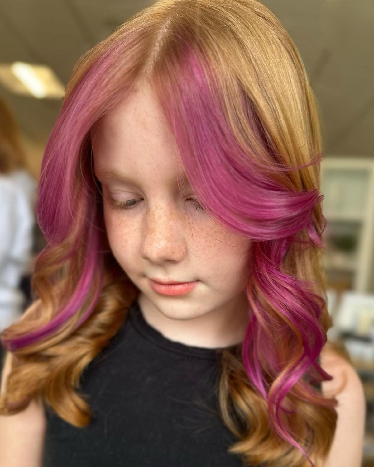 Girl with wavy blonde hair, pink highlights framing her face, and a black top.