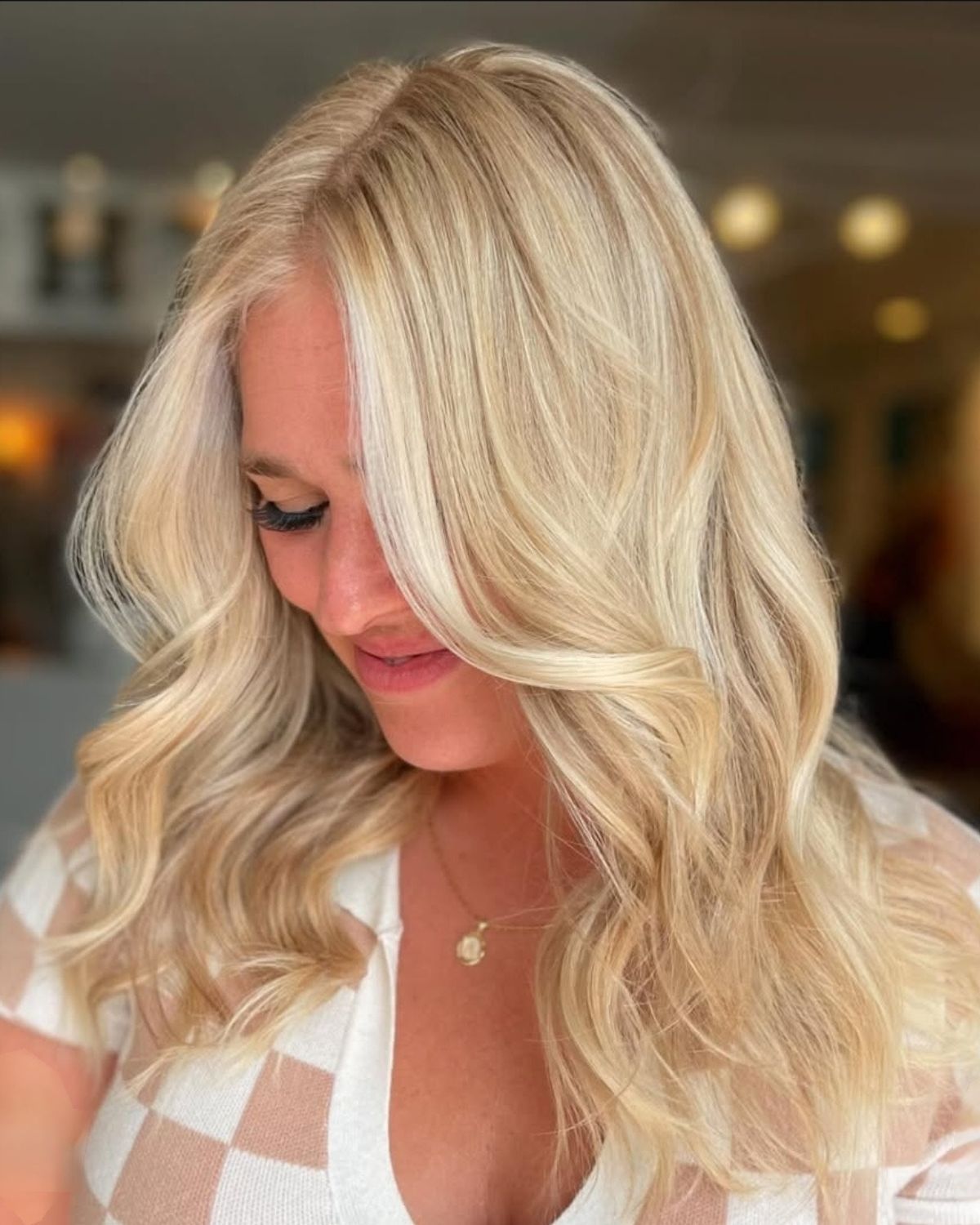 Woman with wavy blonde hair, wearing a white checkered top, smiling.