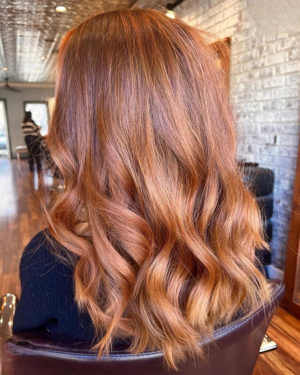 Woman with auburn hair styled in loose waves, sitting in a salon chair.