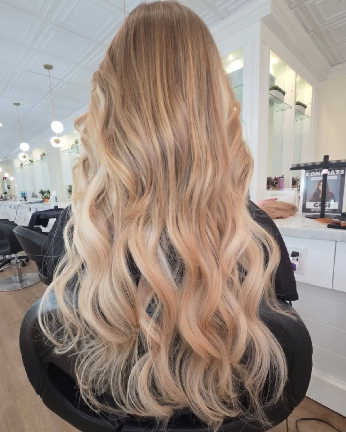 Woman's long, wavy blonde hair with subtle highlights, styled in a salon setting.