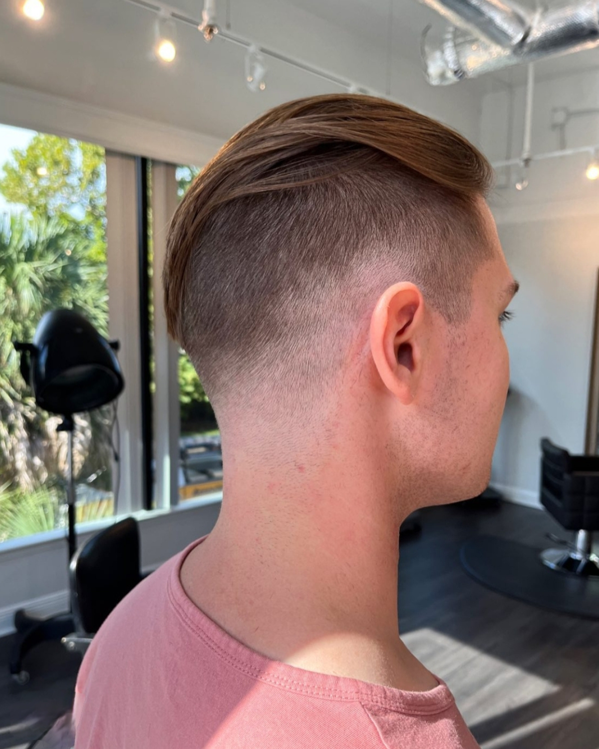 Man with a brown, slicked-back hairstyle and faded sides, in a salon.
