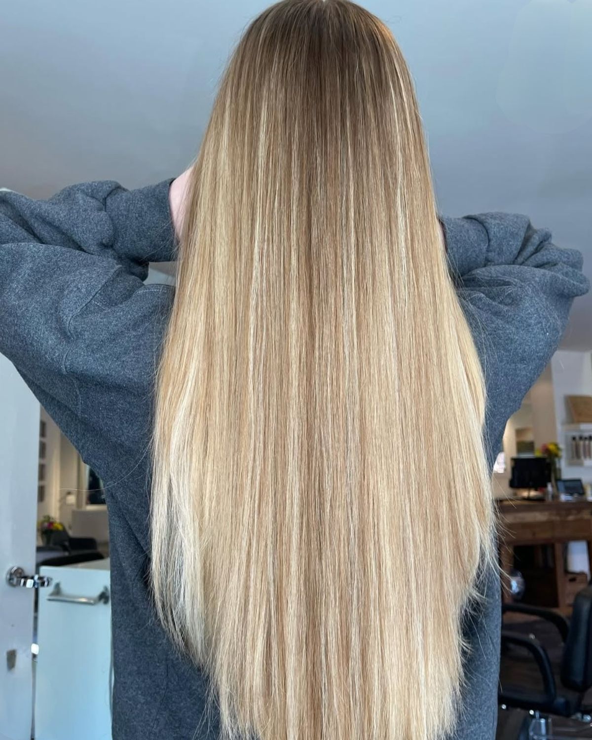 Person with long blonde hair, back to camera, wearing a gray sweatshirt. Hair is straight and shiny.