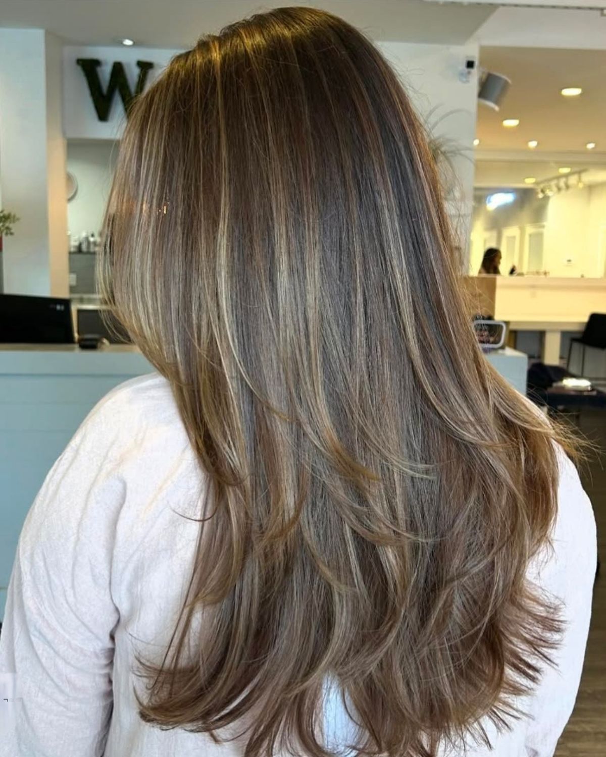 Woman with long brown hair, layered cut, and blonde highlights. Indoors, looking away.