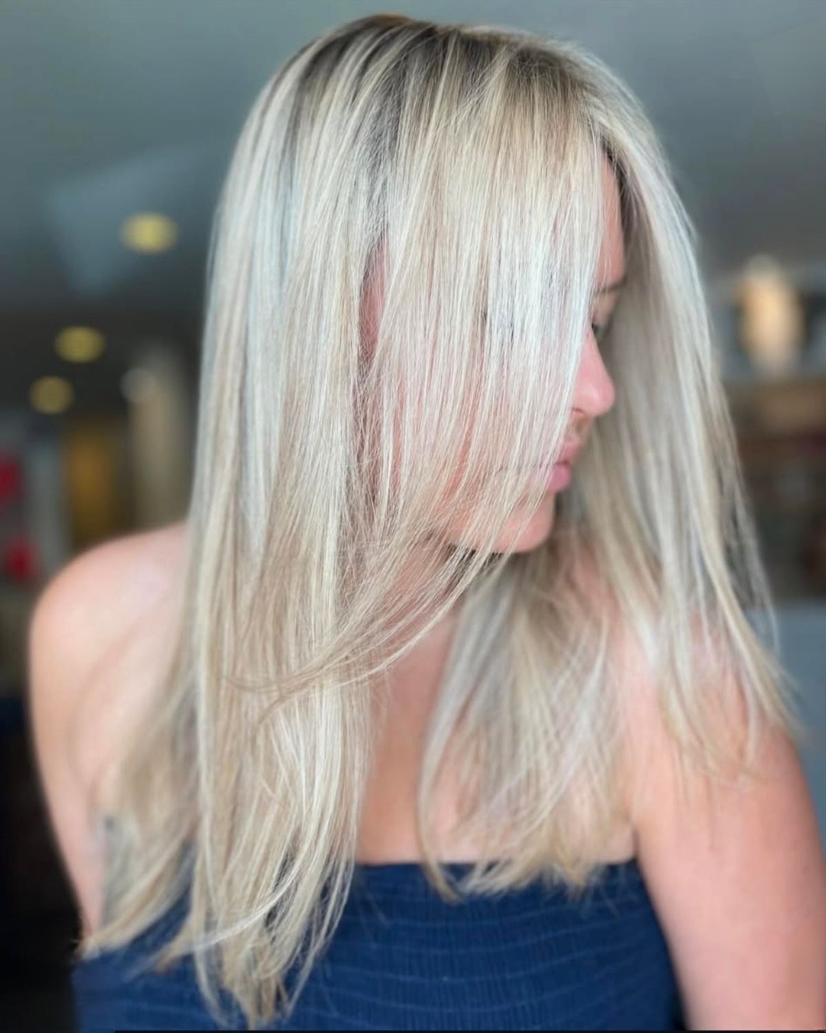 Woman with long, blonde hair, layers framing her face; blue top, blurred background.