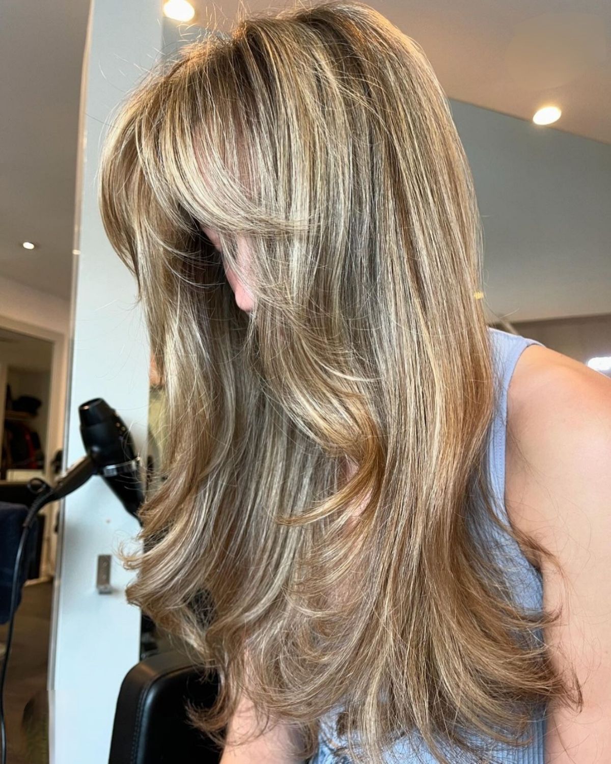 Woman with long blonde and brown layered hair in a salon.