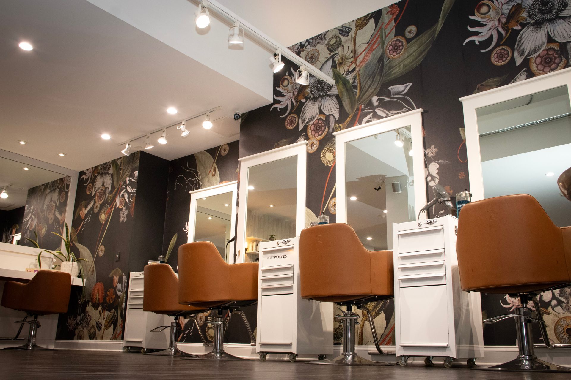 Hair salon interior with brown chairs, mirrors, and floral wallpaper.