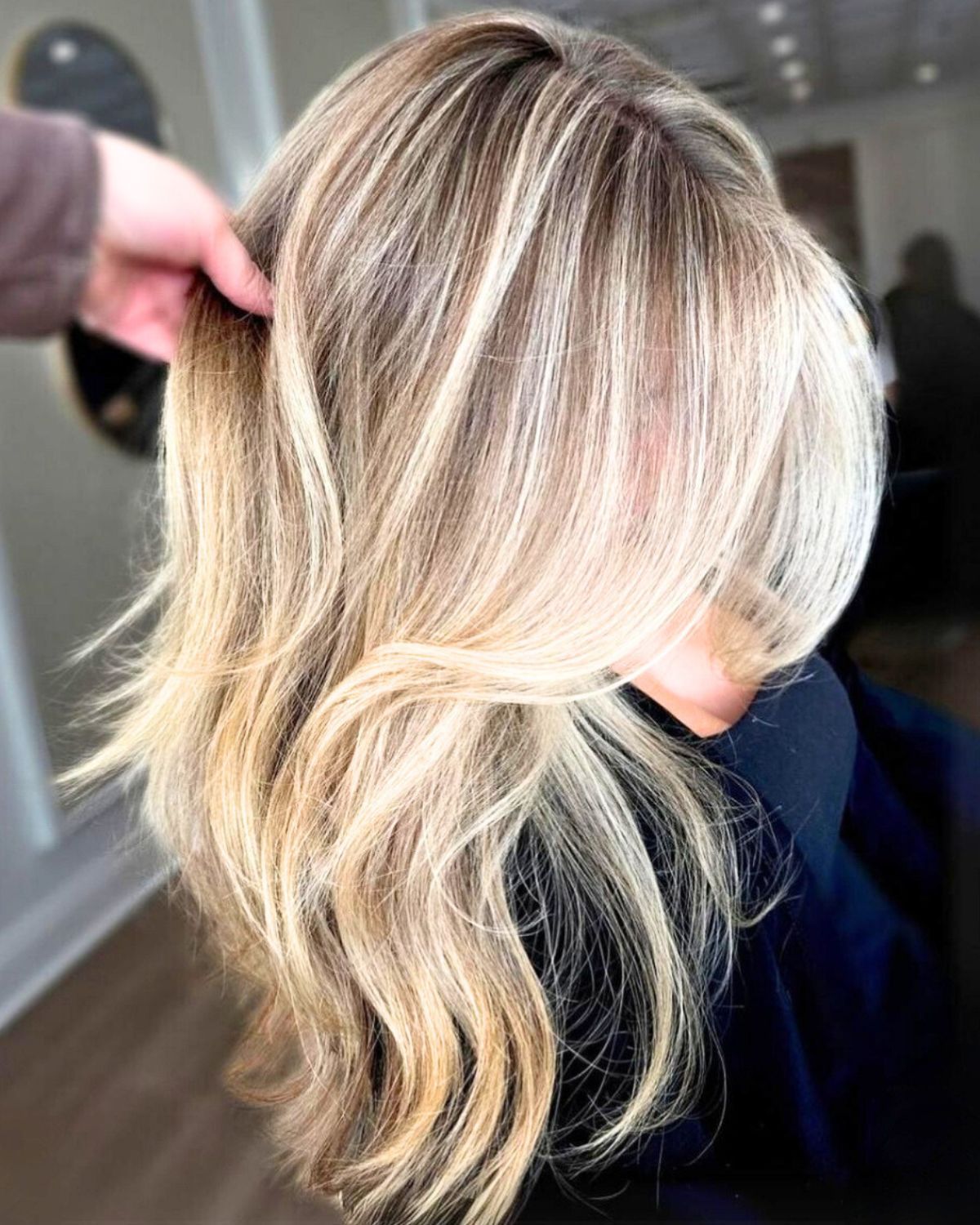 Blonde hair with highlights being held up by a hand in a salon.