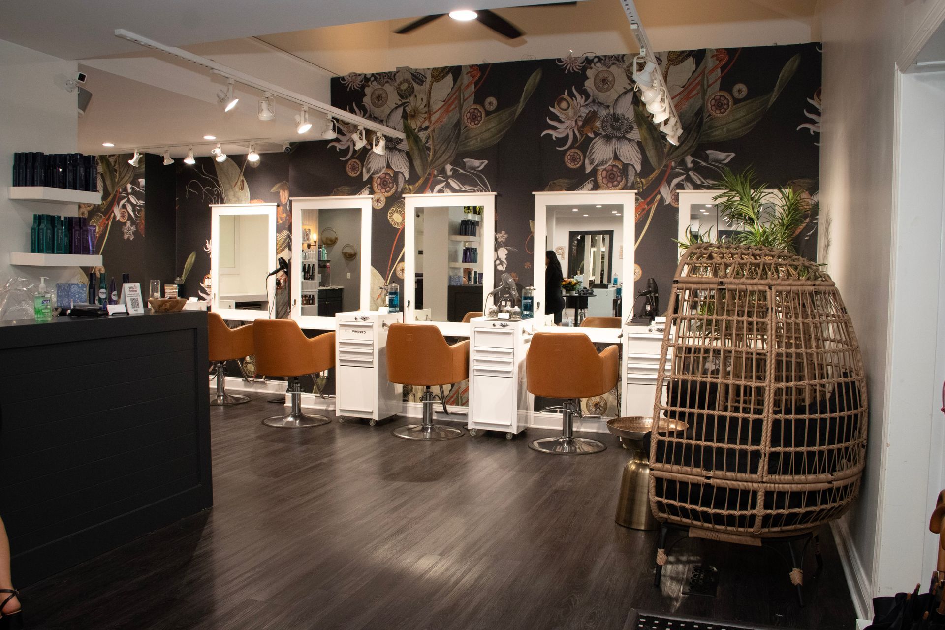 Hair salon interior with styling stations, decorative wallpaper, and a hanging chair.