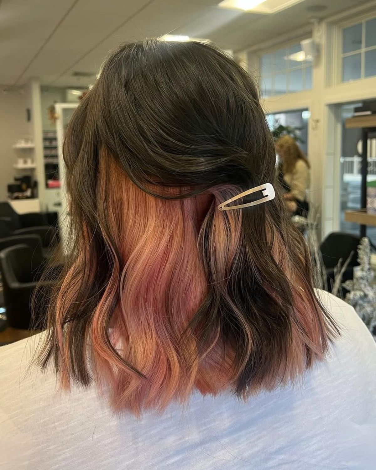 Woman with dark hair, pink highlights, and a gold barrette in a salon.