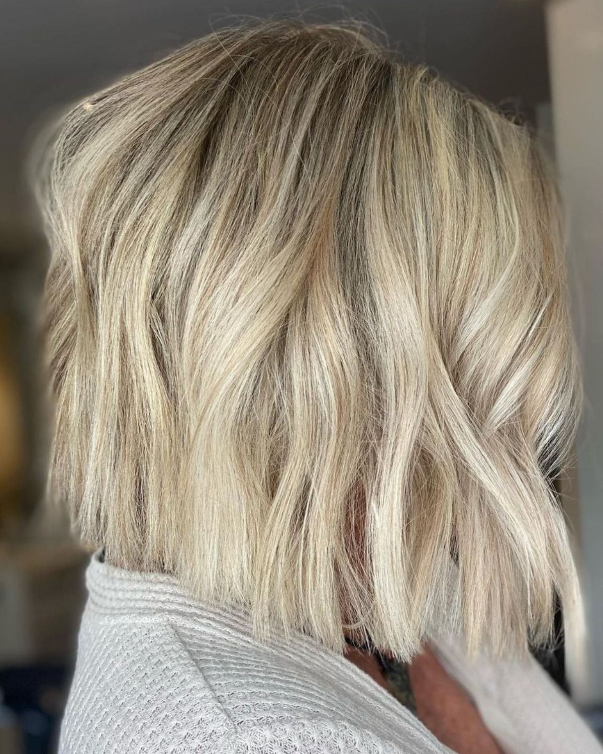 Blonde bob haircut with textured waves, a light-colored top.