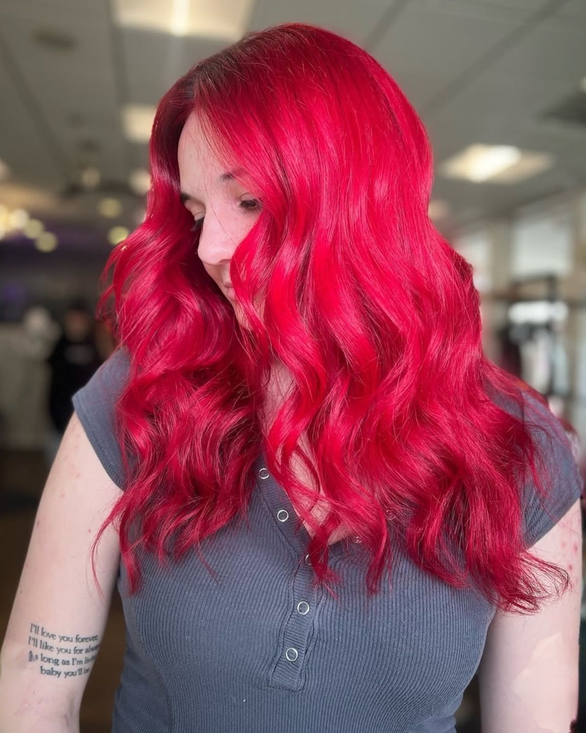 Woman with long, wavy, bright red hair. Wearing a gray shirt, indoors.