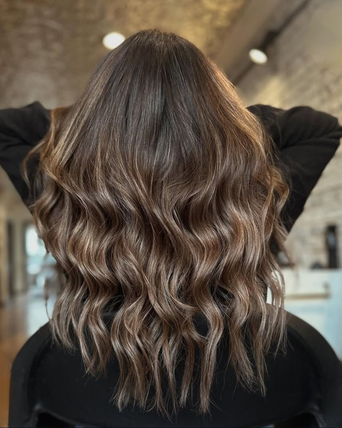 Back view of wavy, medium-length brown hair with lighter highlights, indoors.