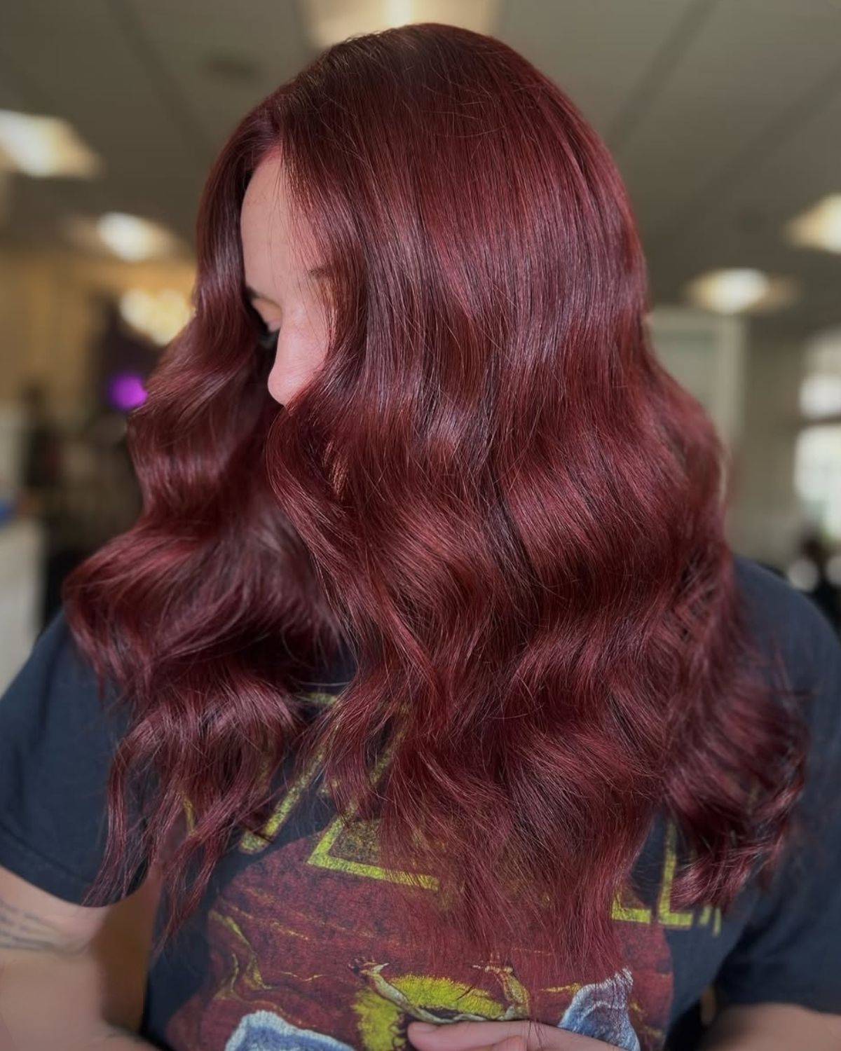 Woman with long, wavy, burgundy hair, wearing a black t-shirt.