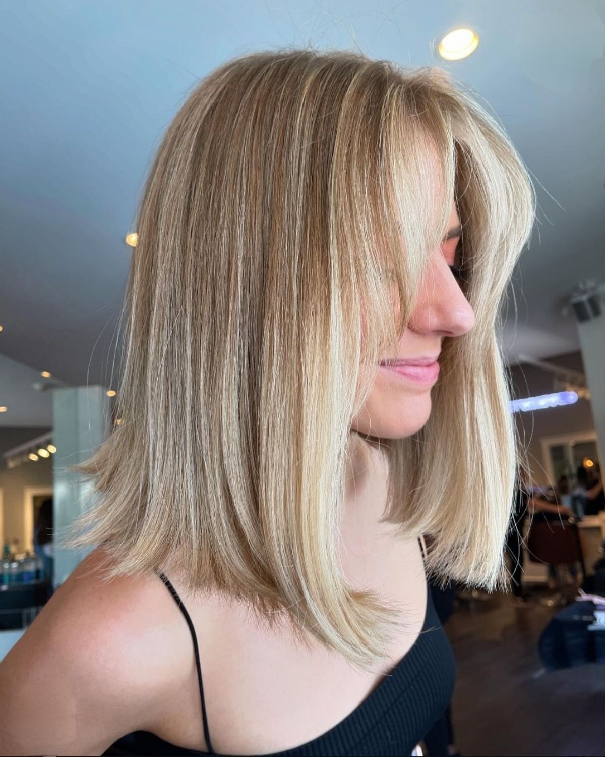 Woman with blonde, shoulder-length hair and side-swept bangs in a salon.