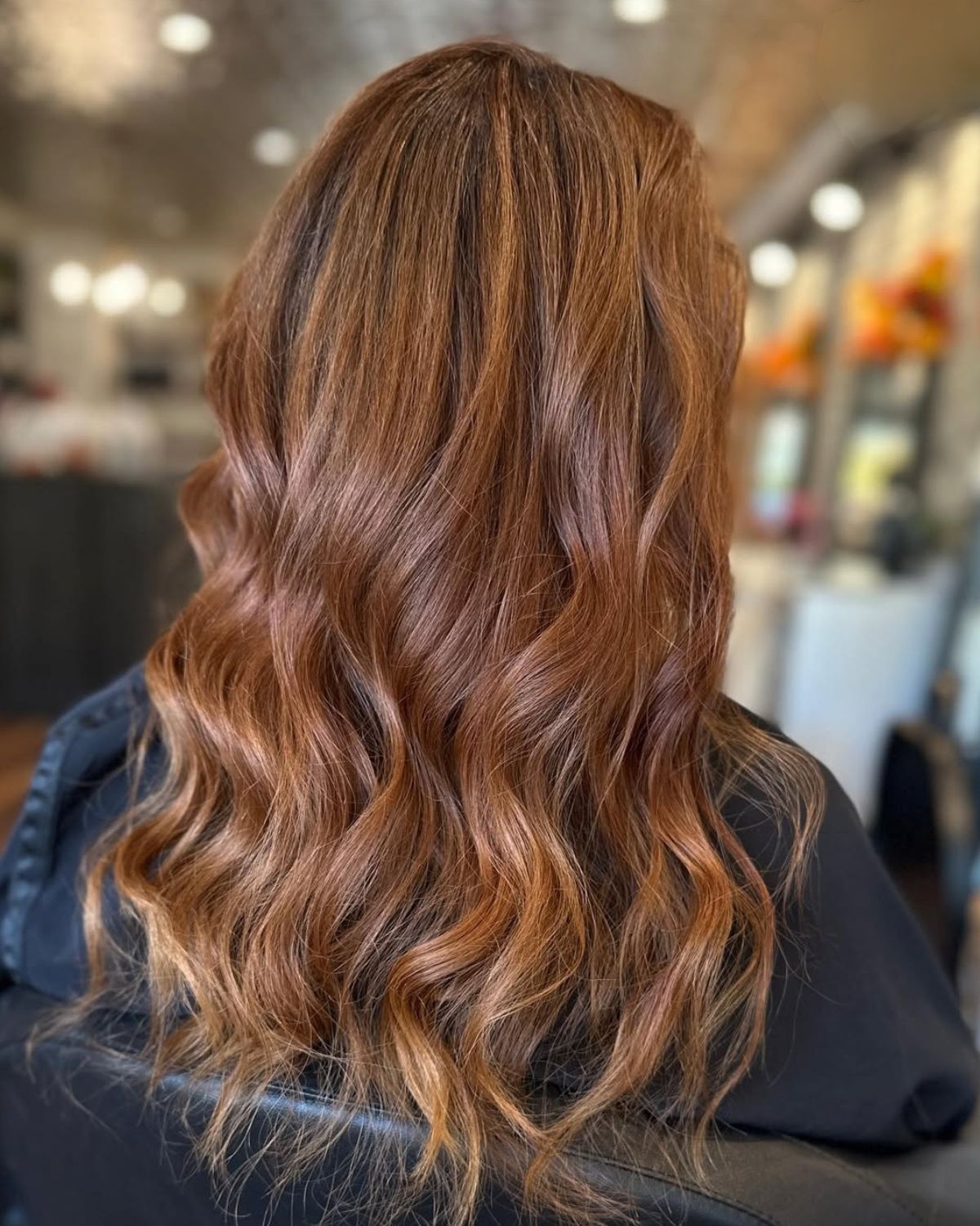 Woman with long, wavy auburn hair. Sitting in a salon chair.