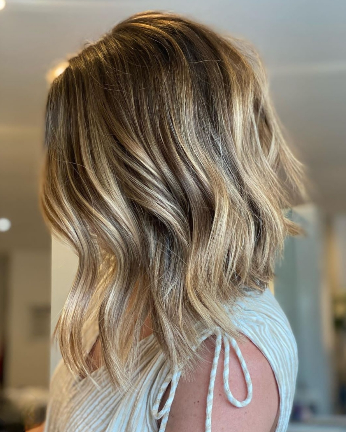 Shoulder-length wavy hair with blonde highlights; subject wearing light top.