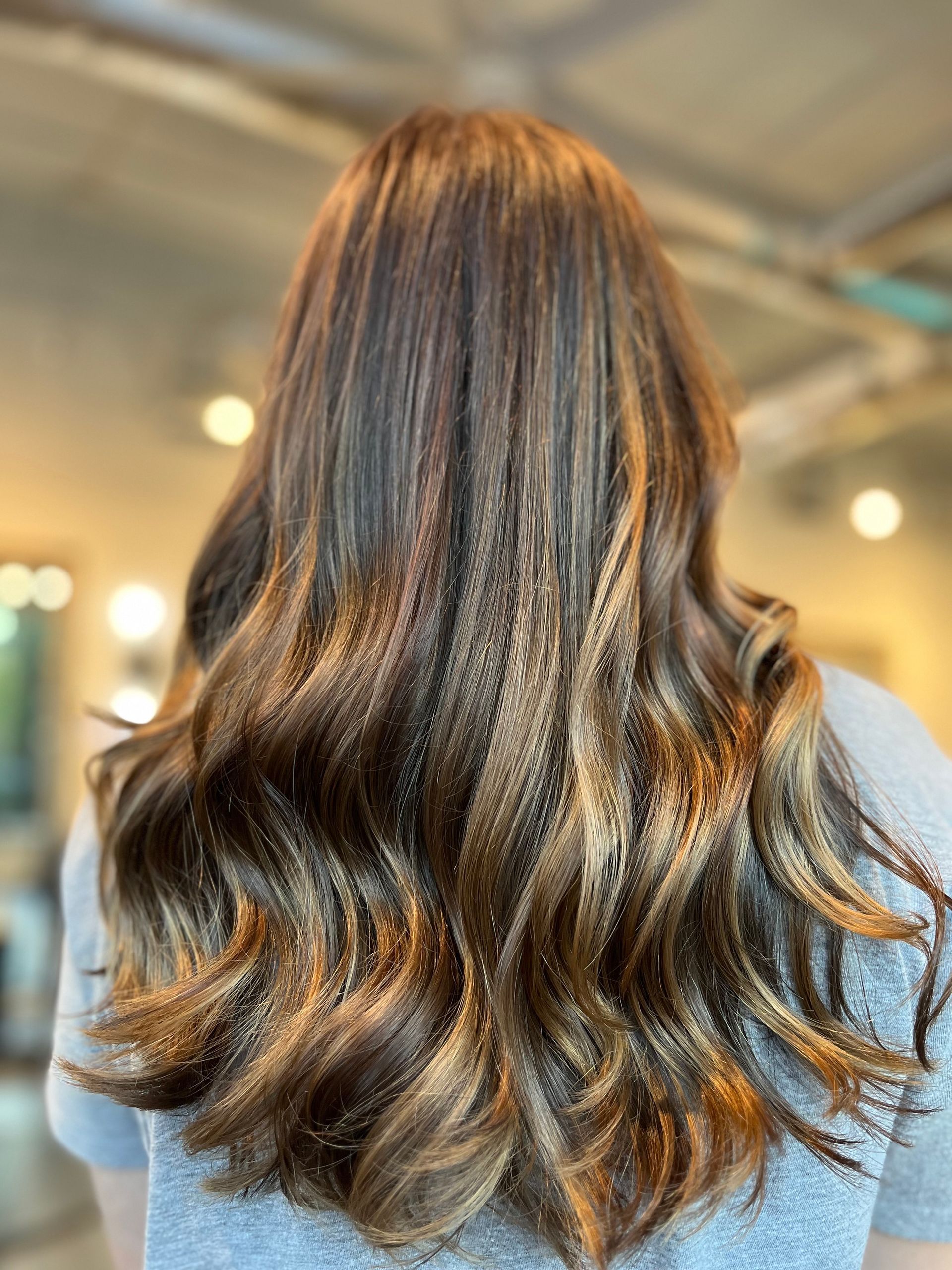 Woman's wavy brown and blonde highlighted hair, viewed from the back, indoors.