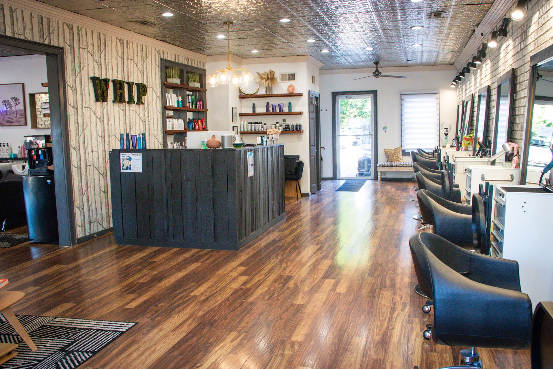 Interior of a hair salon with styling stations, reception desk, products, and a decorative tree design on the wall.