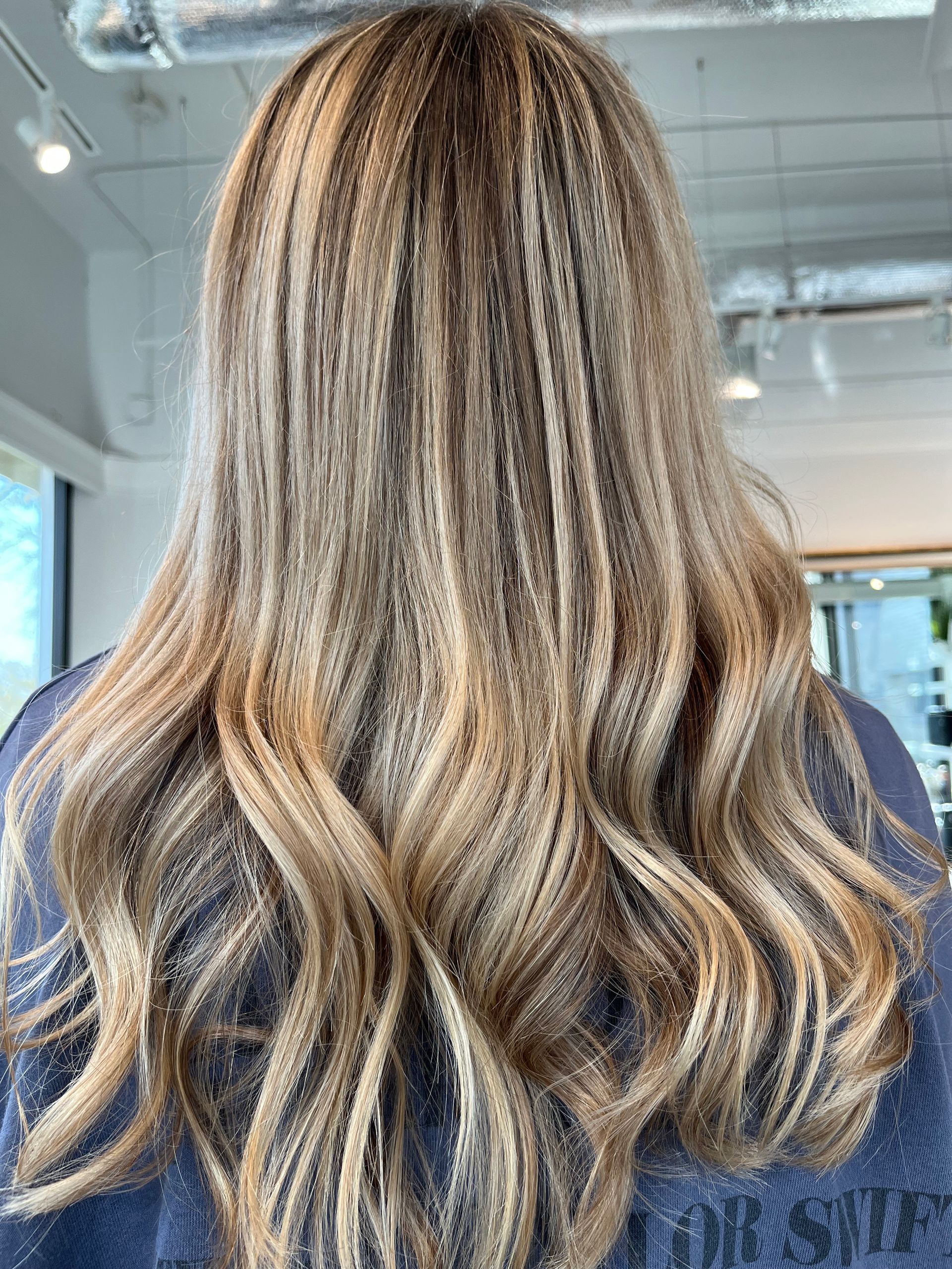 Woman's hair with crimped texture and blonde highlights, wavy ends. Seen from behind.