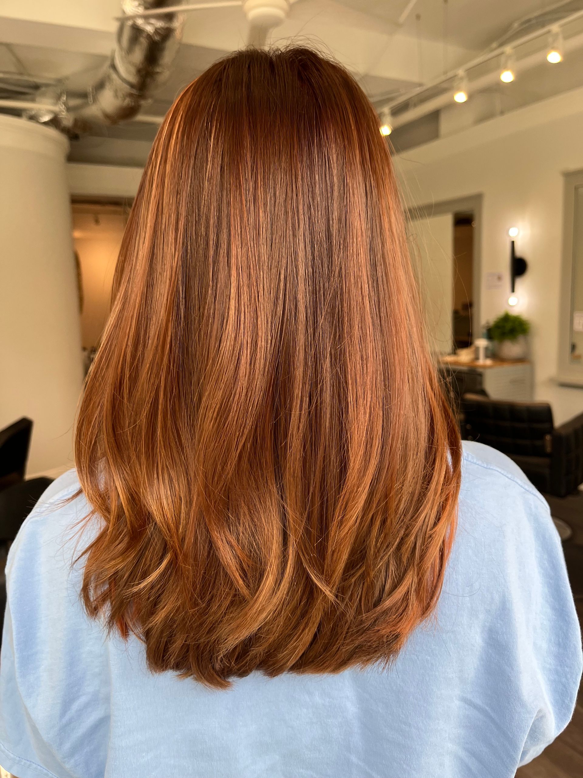 Woman's long, auburn hair styled with loose waves; indoors, lit by daylight.